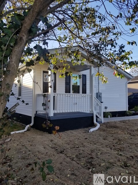 A small white house with a porch and a tree in front.