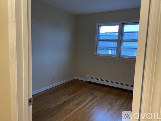 A room with wooden flooring and a window with a view of a building.
