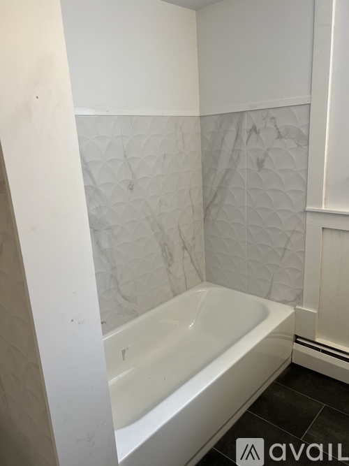 A white bathtub in a bathroom with a white wall and a white tile wall.