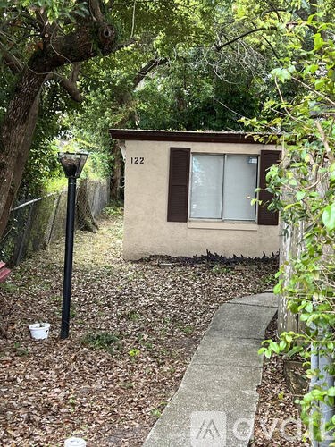 A small house with the number 122 on it is surrounded by trees and has a lamp post in front.