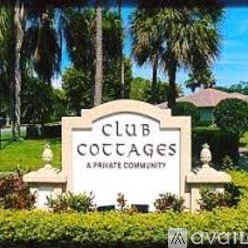 A sign that says Club Cottages in front of some trees.