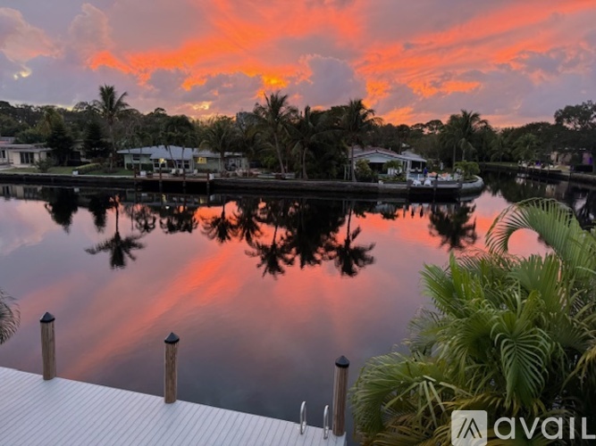 A serene lakeside scene with houses and palm trees reflected in the calm water.