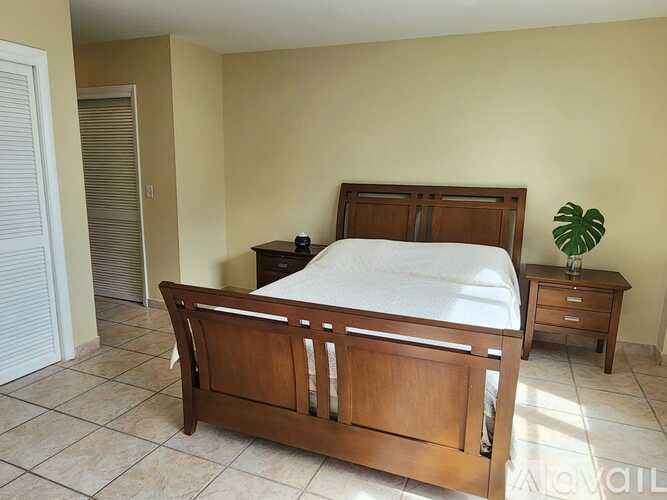 A bedroom with a bed, nightstand, and a plant.