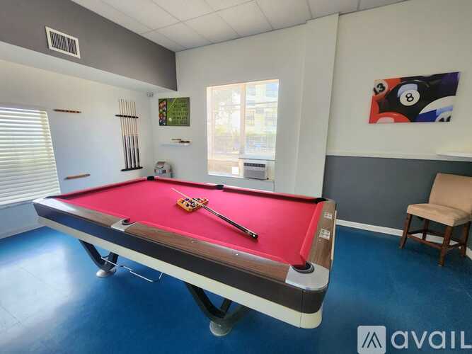 A pool table with a red cloth and a white cue stick is in the middle of the table.