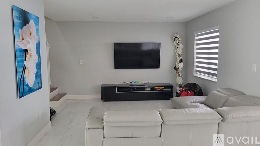 A living room with a white couch and a flat screen TV mounted on the wall.
