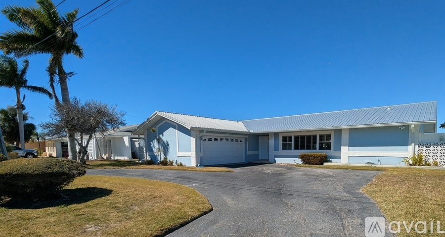 A large blue building with a white garage door is surrounded by a grassy area and palm trees.