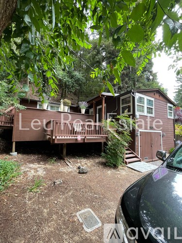 A house with a brown exterior and a deck is surrounded by trees.