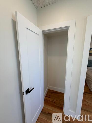 A white door with a black handle is open to a room with a bed.
