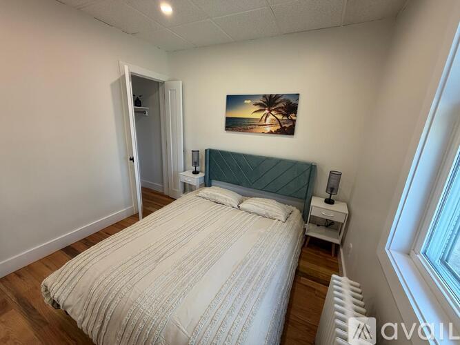 A bedroom with a bed, nightstand, and a painting on the wall.