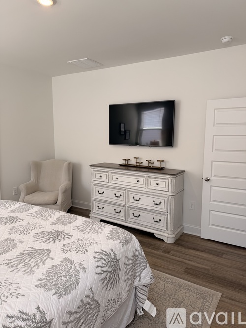 A bedroom with a bed, a chair, a dresser, and a flat-screen TV mounted on the wall.