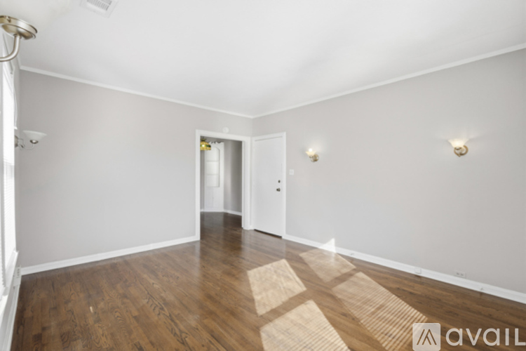 A room with wooden floors and white walls, with a doorway leading to another room.