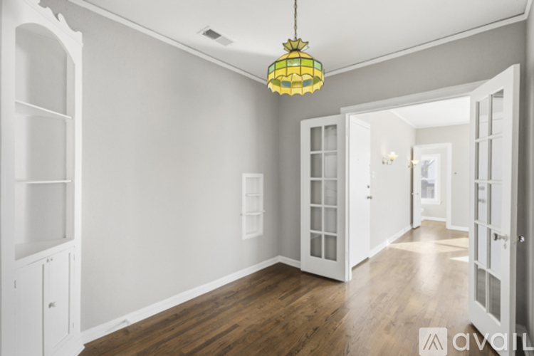 A room with a wooden floor and white walls, with a hanging light fixture and a doorway leading to another room.