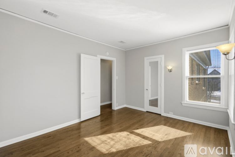 A room with wooden floors and white walls, with a window showing a building outside.