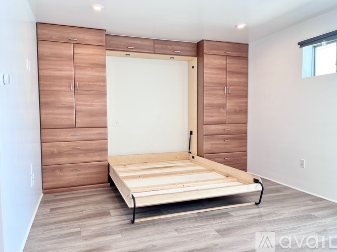 A bedroom with a bed, wooden floor, and a wall of cabinets.