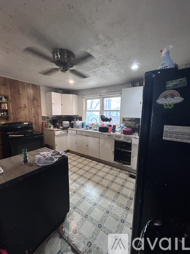 A kitchen with a black fridge and a ceiling fan.
