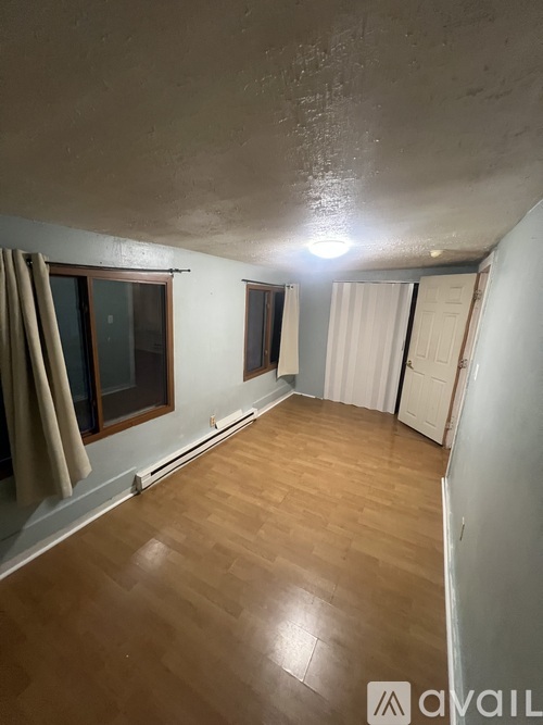 A room with wooden flooring and a window with curtains.