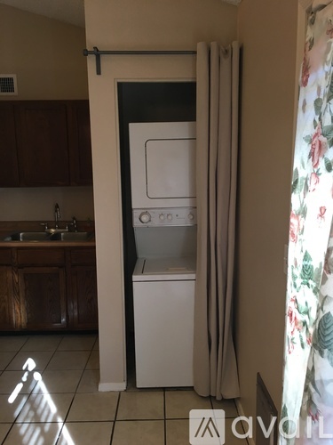 A white dishwasher is in a kitchen with a window covered in floral curtains.