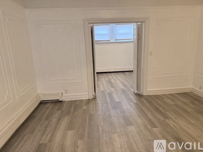 A room with white walls and wooden flooring with a window.
