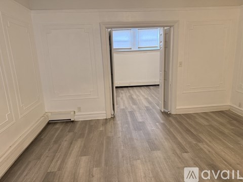 A room with white walls and wooden flooring with a window.