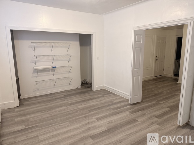 A room with a white wall and a grey floor with a shelf on the wall.