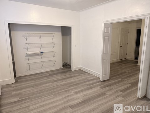 A room with a white wall and a grey floor with a shelf on the wall.