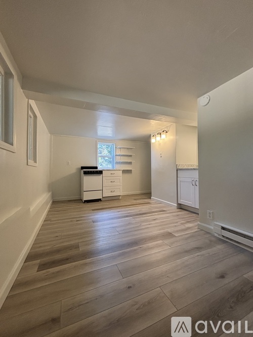 A spacious room with wooden flooring and white walls.