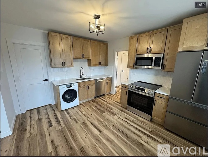 A kitchen with wooden floors and cabinets, a washing machine, and a refrigerator.