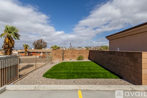 A backyard with a green lawn and a brown wall.