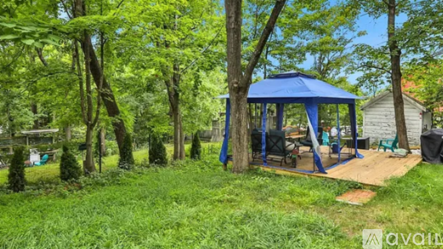 A blue gazebo is surrounded by trees in a grassy area.
