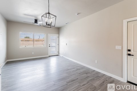 A spacious room with a large window, hardwood floors, and a hanging light fixture.