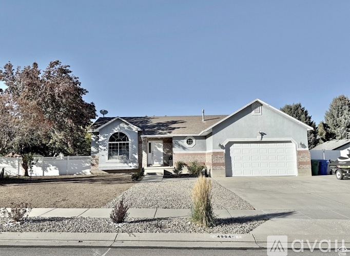A house with a white garage door is surrounded by a white fence and has a tree in front of it.