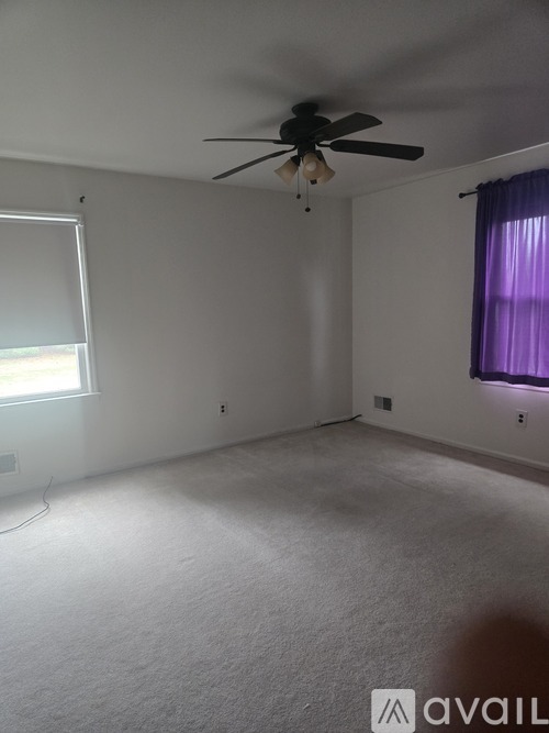 A room with a ceiling fan and a window with purple curtains.