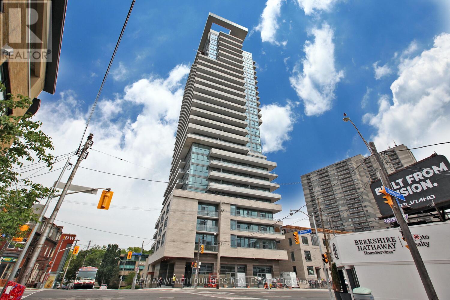 A tall building with a curved top is in the middle of a city street.