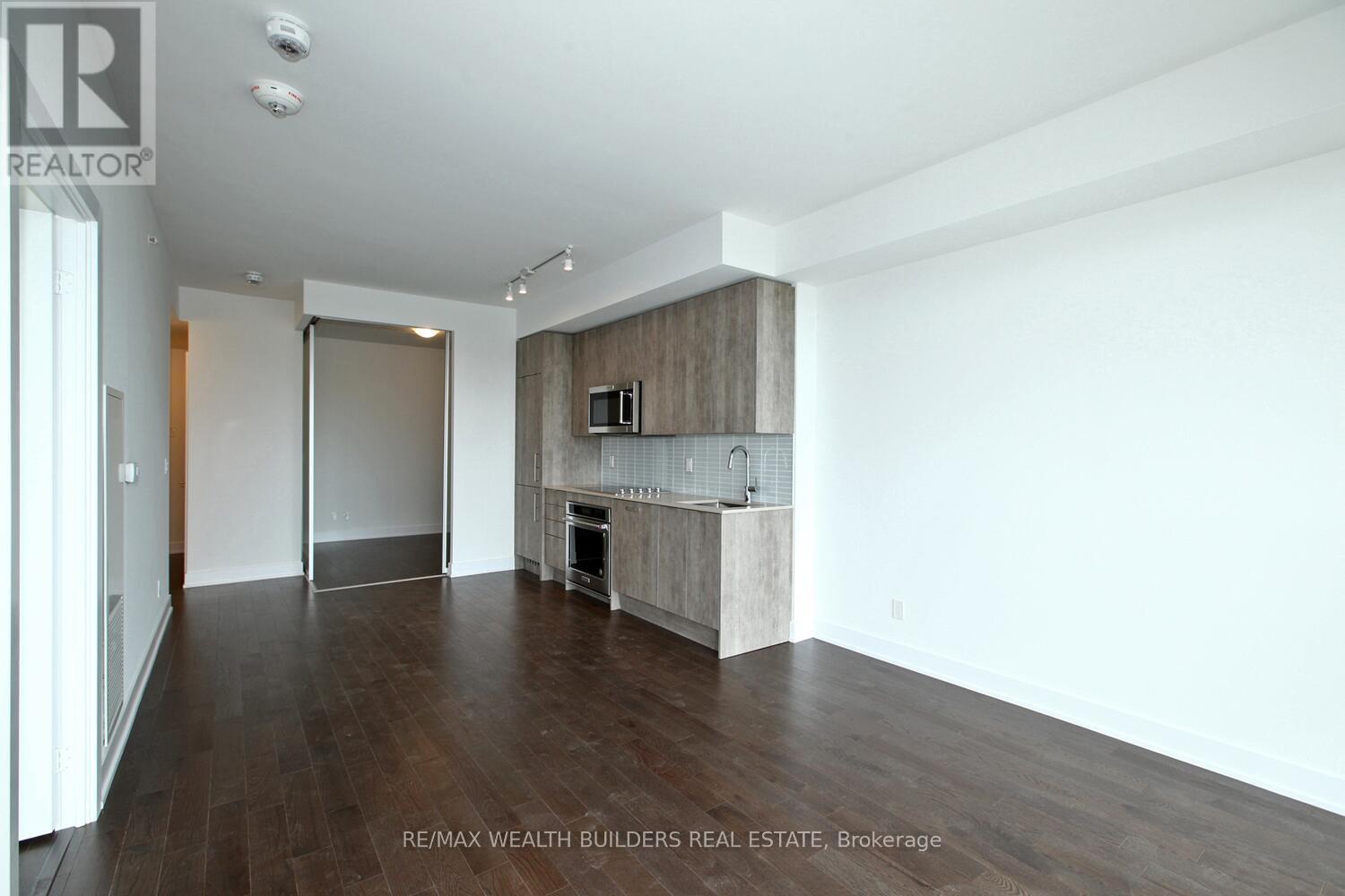 A spacious room with wooden floors and a kitchen area with white cabinets and appliances.