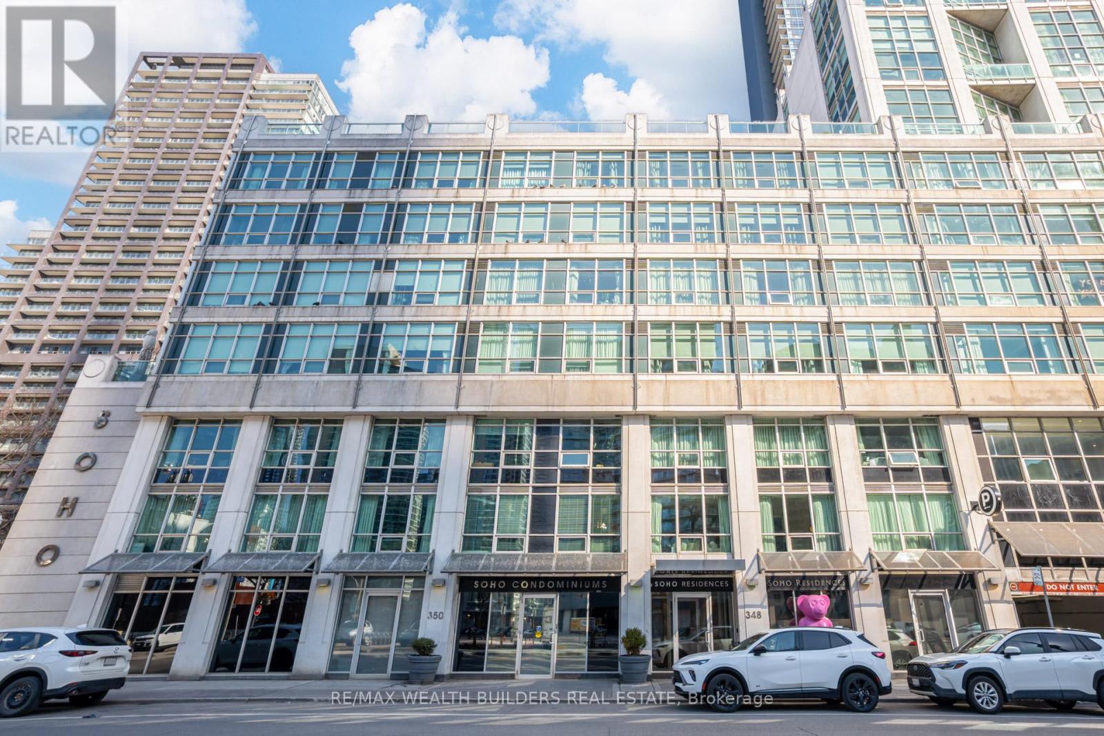 A pink bear statue is in front of a building with the sign "Soho Residences".