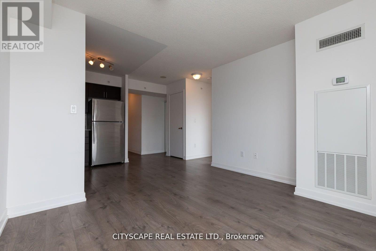 A spacious room with a stainless steel refrigerator and wooden flooring.