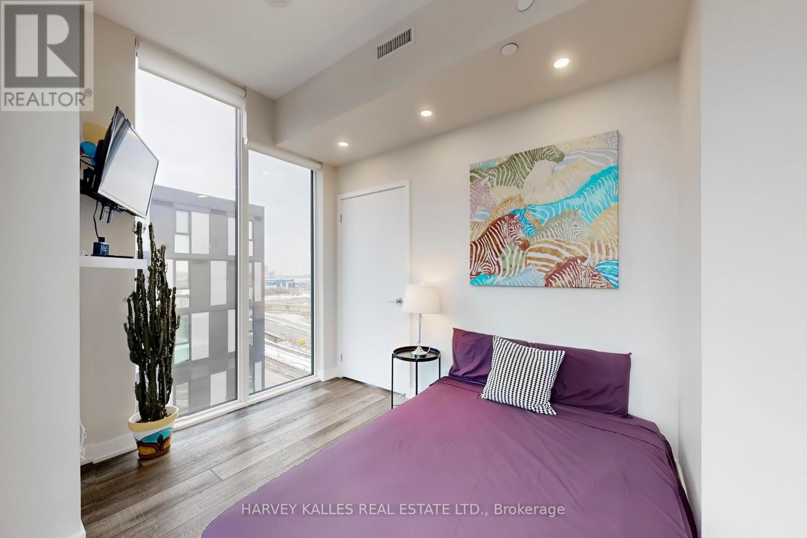 A bedroom with a purple bed and a painting on the wall.