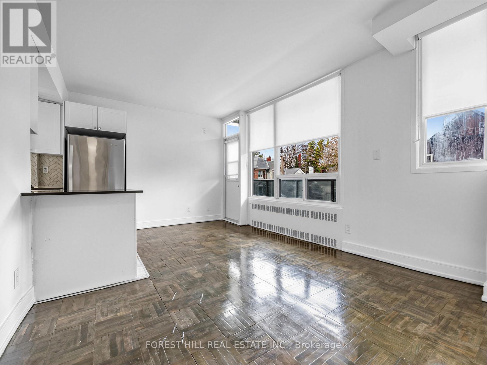 A spacious room with wooden flooring and large windows.