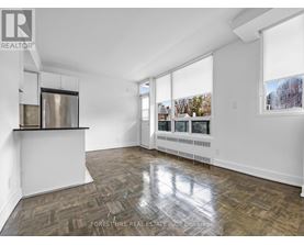 A spacious room with wooden flooring and large windows.