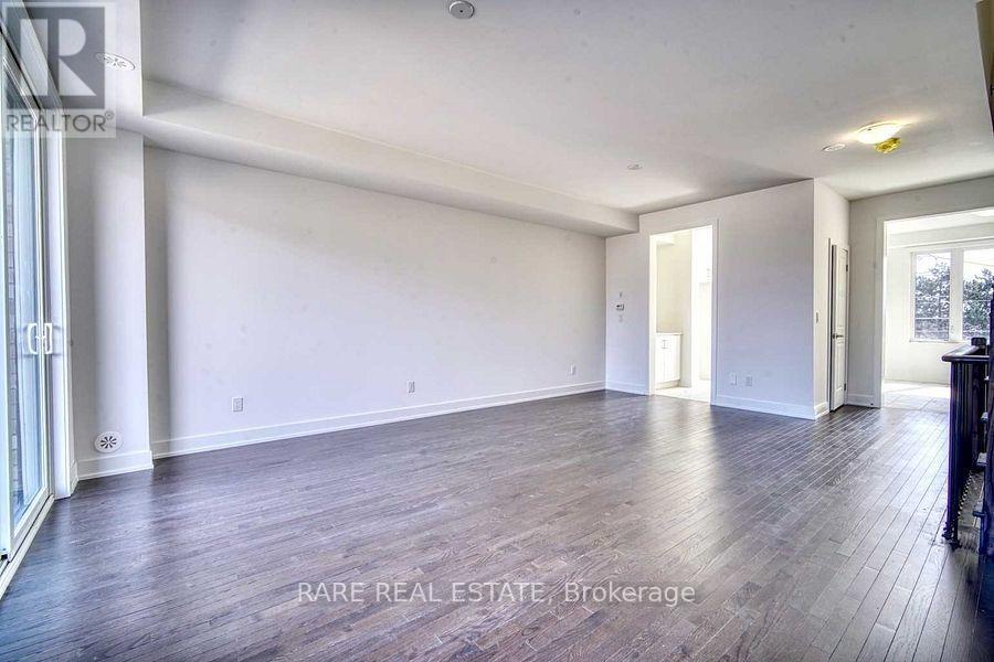 A spacious room with wood flooring and white walls, labeled as a rare real estate brokerage.