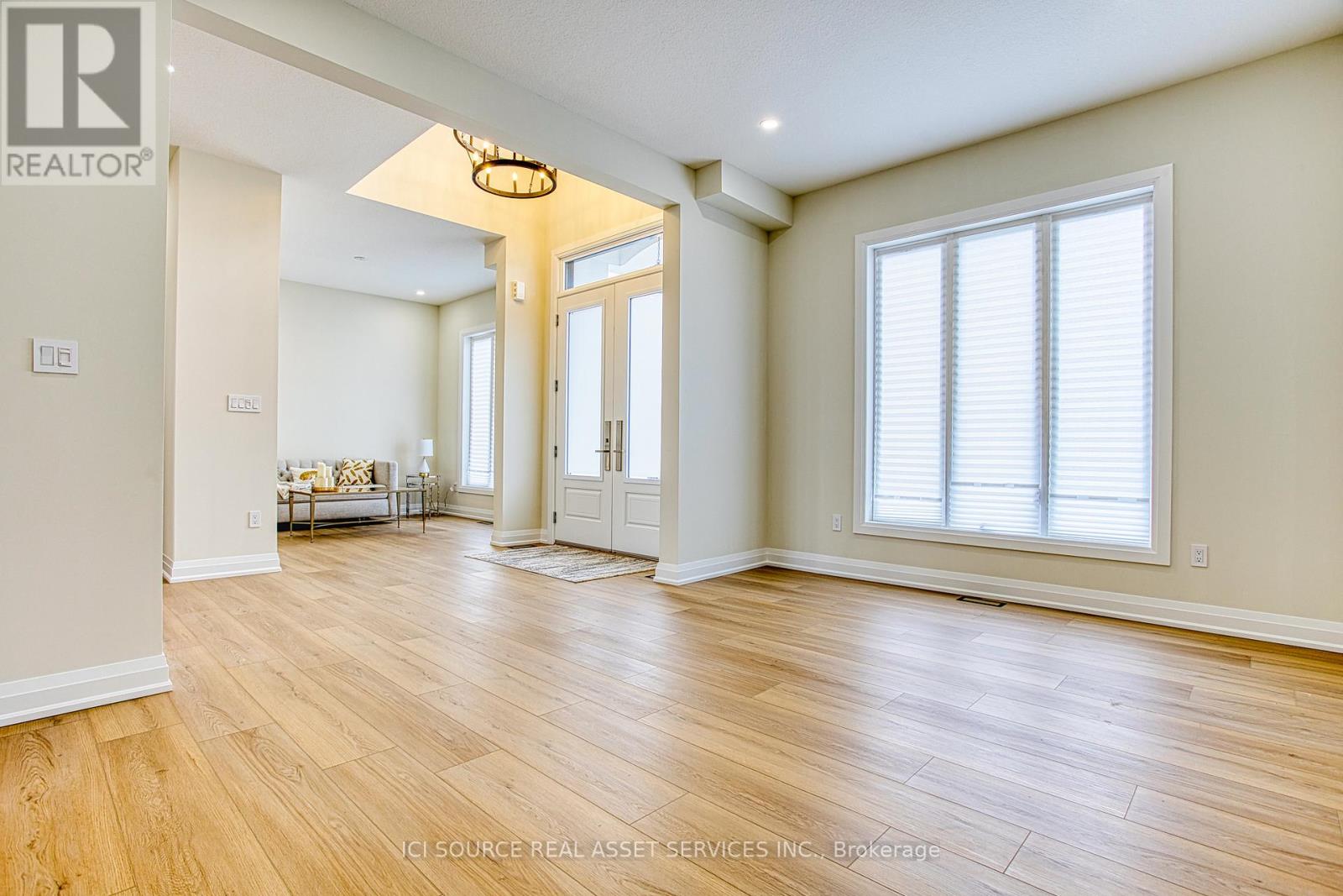 A spacious room with wooden flooring and a large window with white blinds.