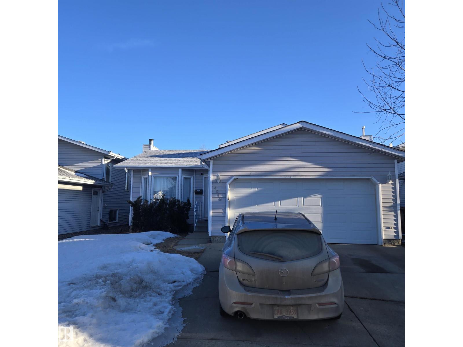A car is parked in front of a house with a garage.