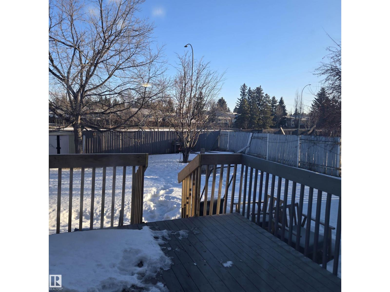 A deck with snow on the ground and trees in the background.