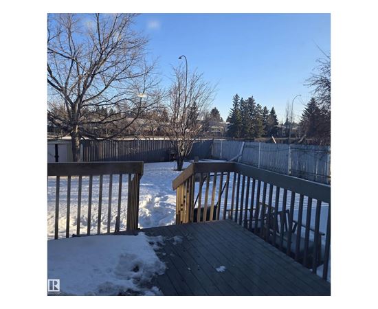 A deck with snow on the ground and trees in the background.