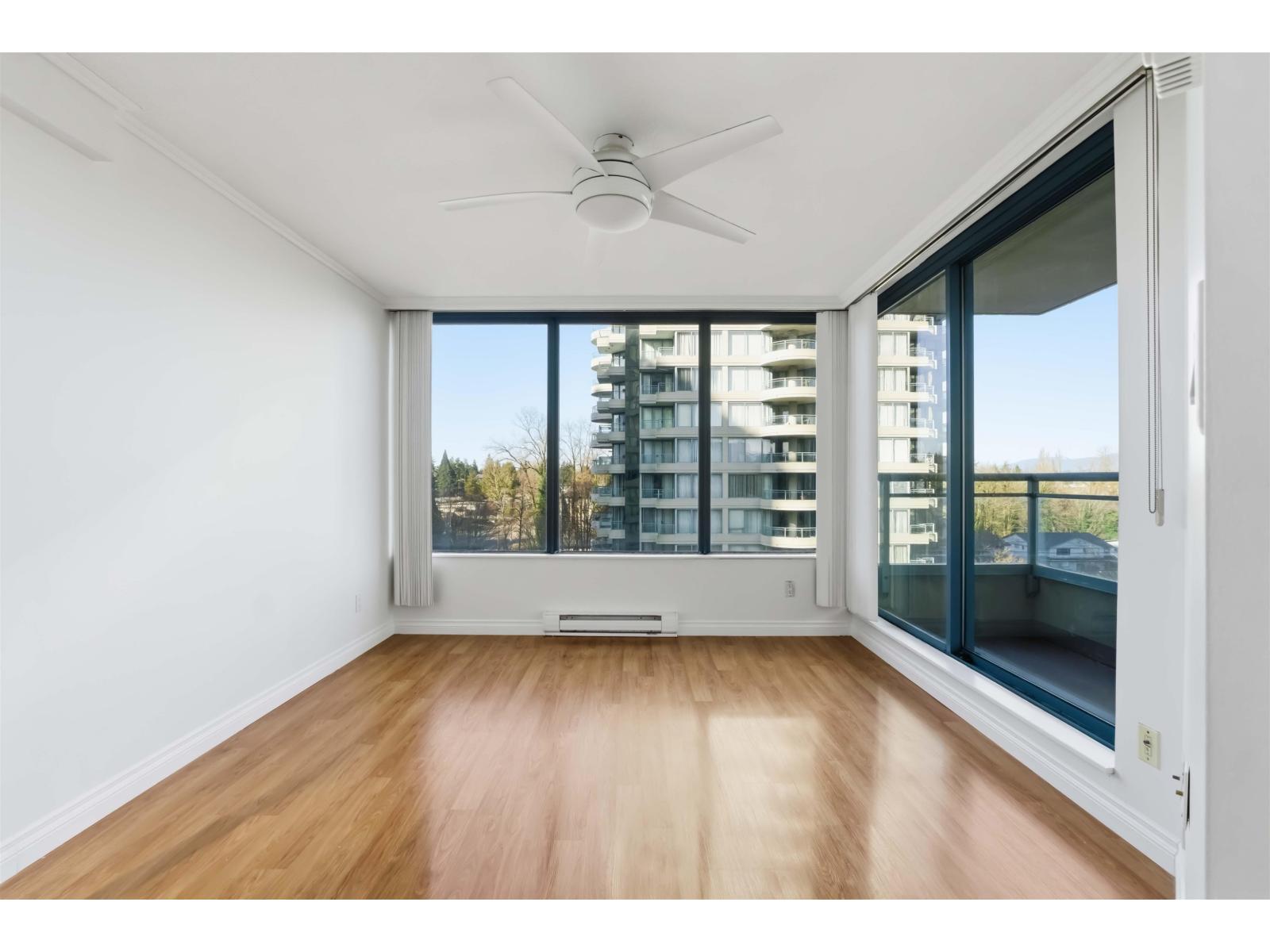 A room with a ceiling fan and a view of a building outside the window.