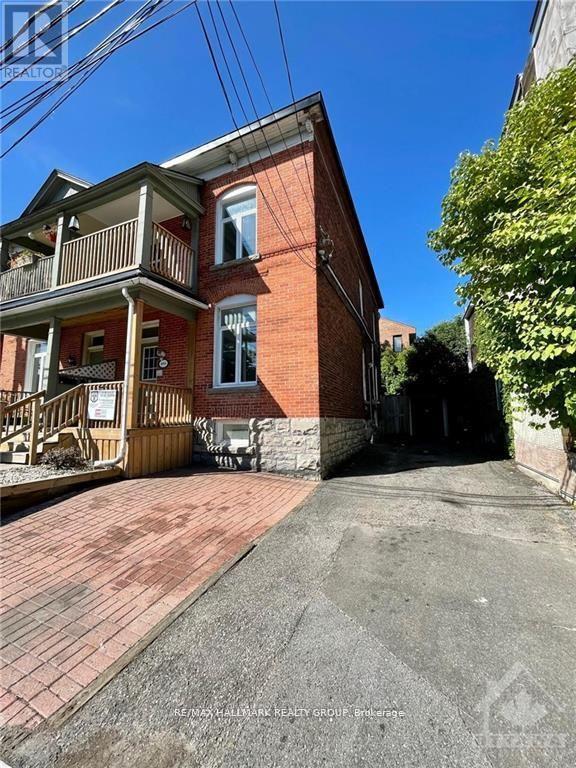 A red brick house with a balcony and a driveway in front.