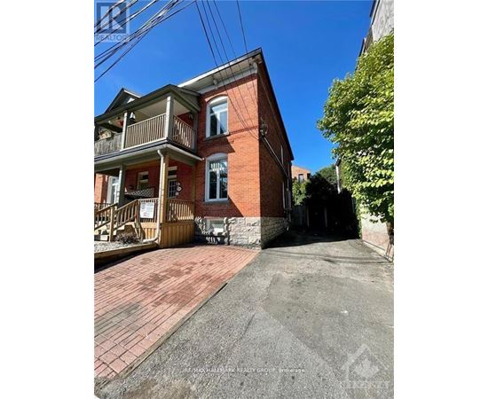 A red brick house with a balcony and a driveway in front.