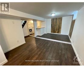 A spacious room with wood flooring and a staircase leading to the upper level.