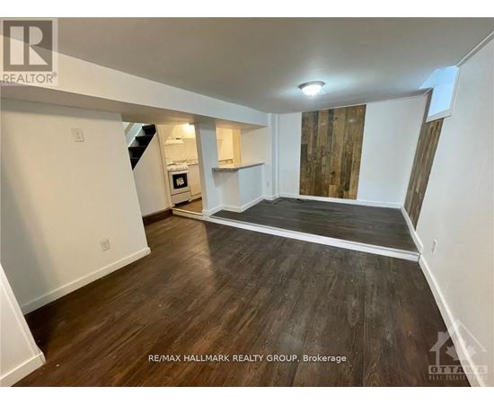 A spacious room with wood flooring and a staircase leading to the upper level.
