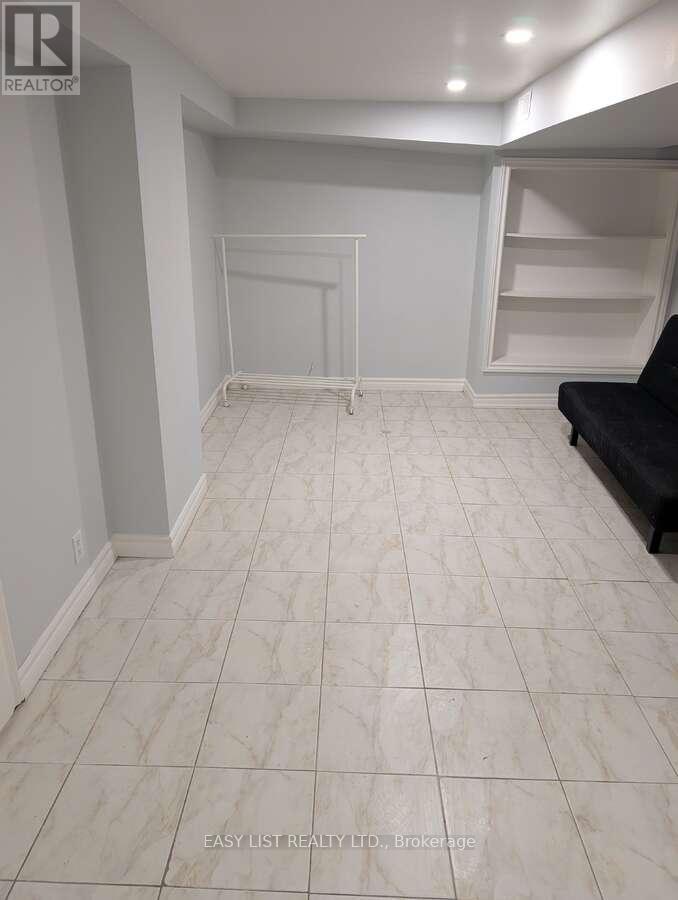A spacious room with white tiled flooring and a black couch.
